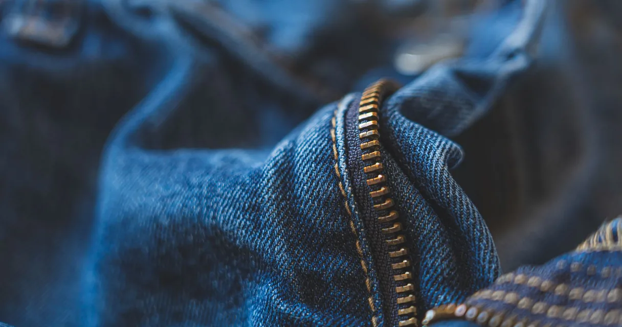 Zíper dourado em um tecido jeans, ilustrando como consertar um zíper